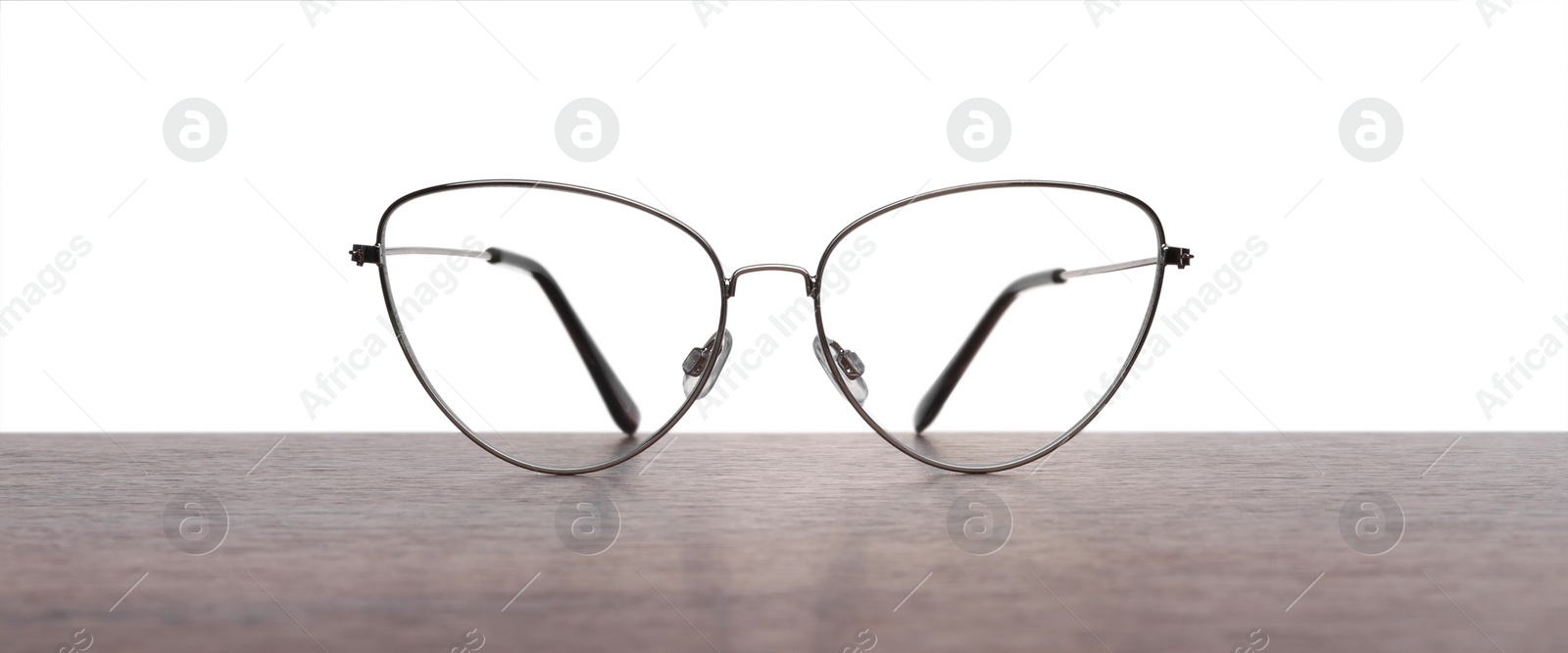 Photo of Stylish glasses with metal frame on wooden table against white background