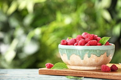 Bowl with delicious ripe raspberries on wooden table against blurred background, space for text