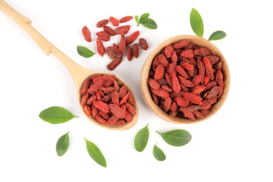 Wooden bowl and spoon of dried goji berries with leaves on white background, top view