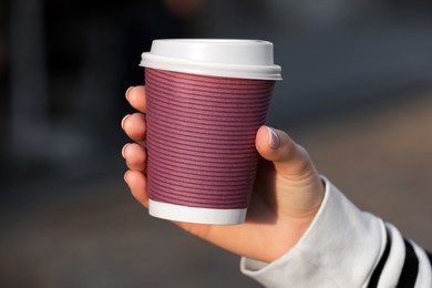 Photo of Woman holding paper takeaway cup outdoors, closeup. Coffee to go