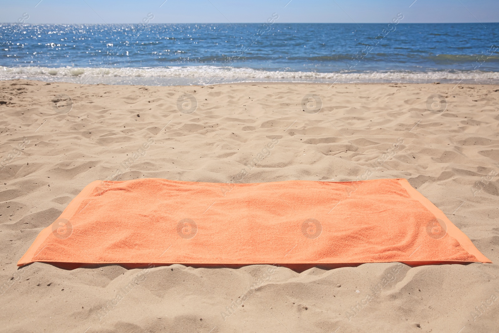 Photo of Soft orange beach towel on sandy seashore