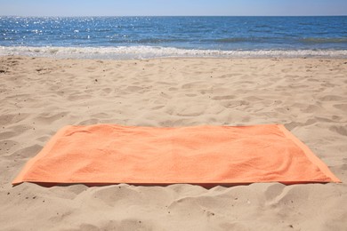 Photo of Soft orange beach towel on sandy seashore