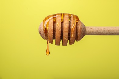 Delicious honey flowing down from dipper against yellow background, closeup. Space for text