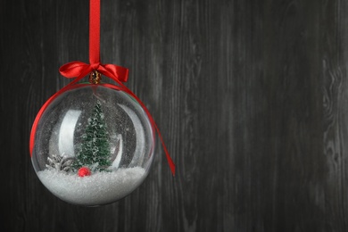 Photo of Beautiful Christmas snow globe hanging on black wooden background, space for text