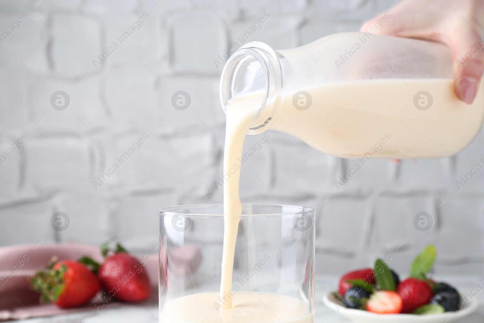 Photo of Woman pouring tasty yogurt into glass at table, closeup