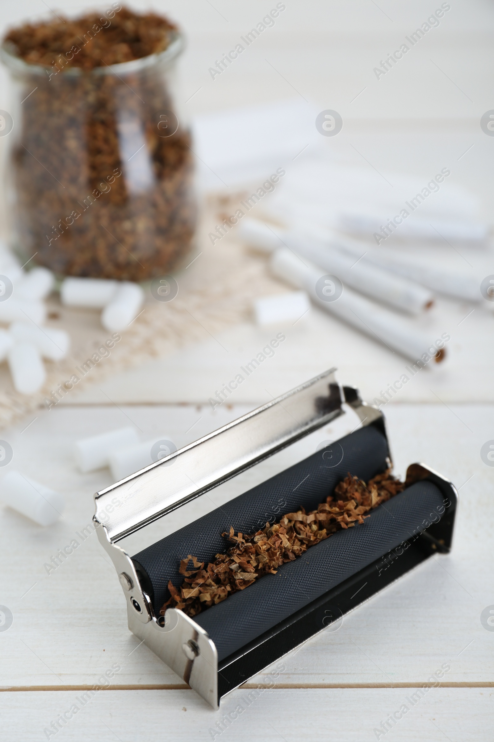 Photo of Roller with tobacco on white wooden table. Making hand rolled cigarettes