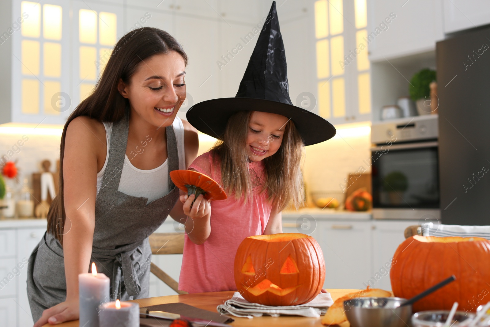 Photo of Mother and daughter making pumpkin jack o'lantern at table in kitchen. Halloween celebration