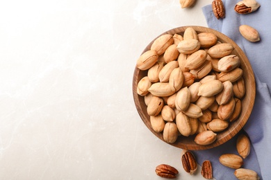 Photo of Ripe pecan nuts in dish served on light table, flat lay. Space for text