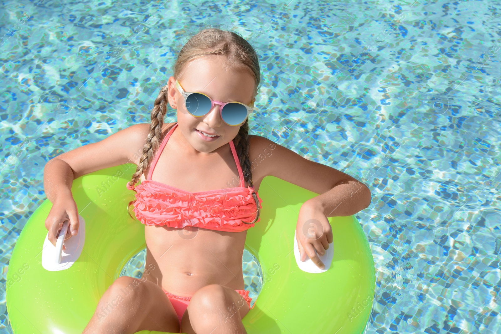 Photo of Cute little girl with sunglasses and inflatable ring in pool on sunny day