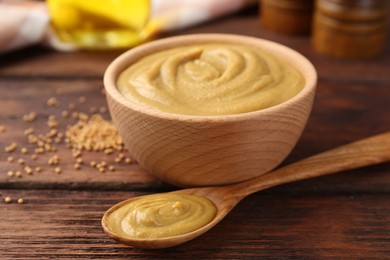 Photo of Bowl and spoon with tasty mustard sauce on wooden table, closeup
