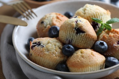 Photo of Delicious muffins with blueberries and mint in bowl on table, closeup