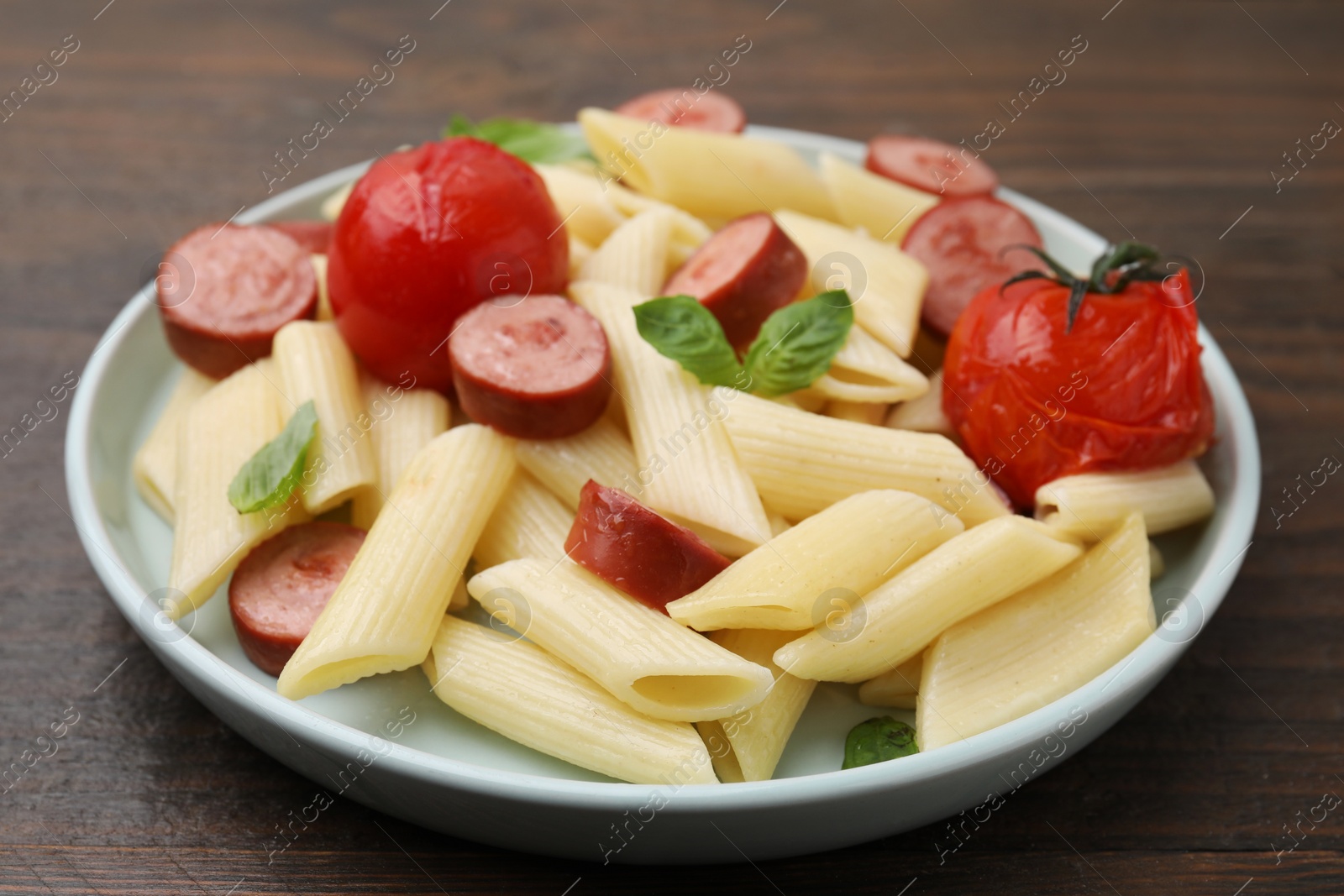Photo of Tasty pasta with smoked sausage, tomatoes and basil on wooden table, closeup