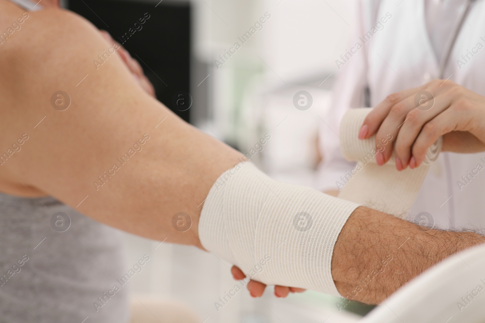 Photo of Orthopedist applying bandage onto patient's elbow in clinic, closeup