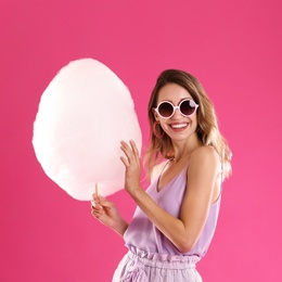 Photo of Happy young woman with cotton candy on pink background