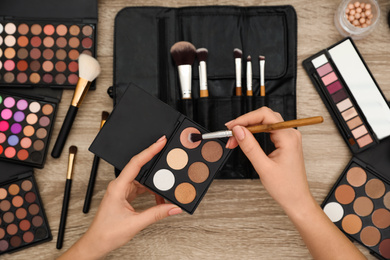 Professional makeup artist with eyeshadow and brush at wooden table, top view