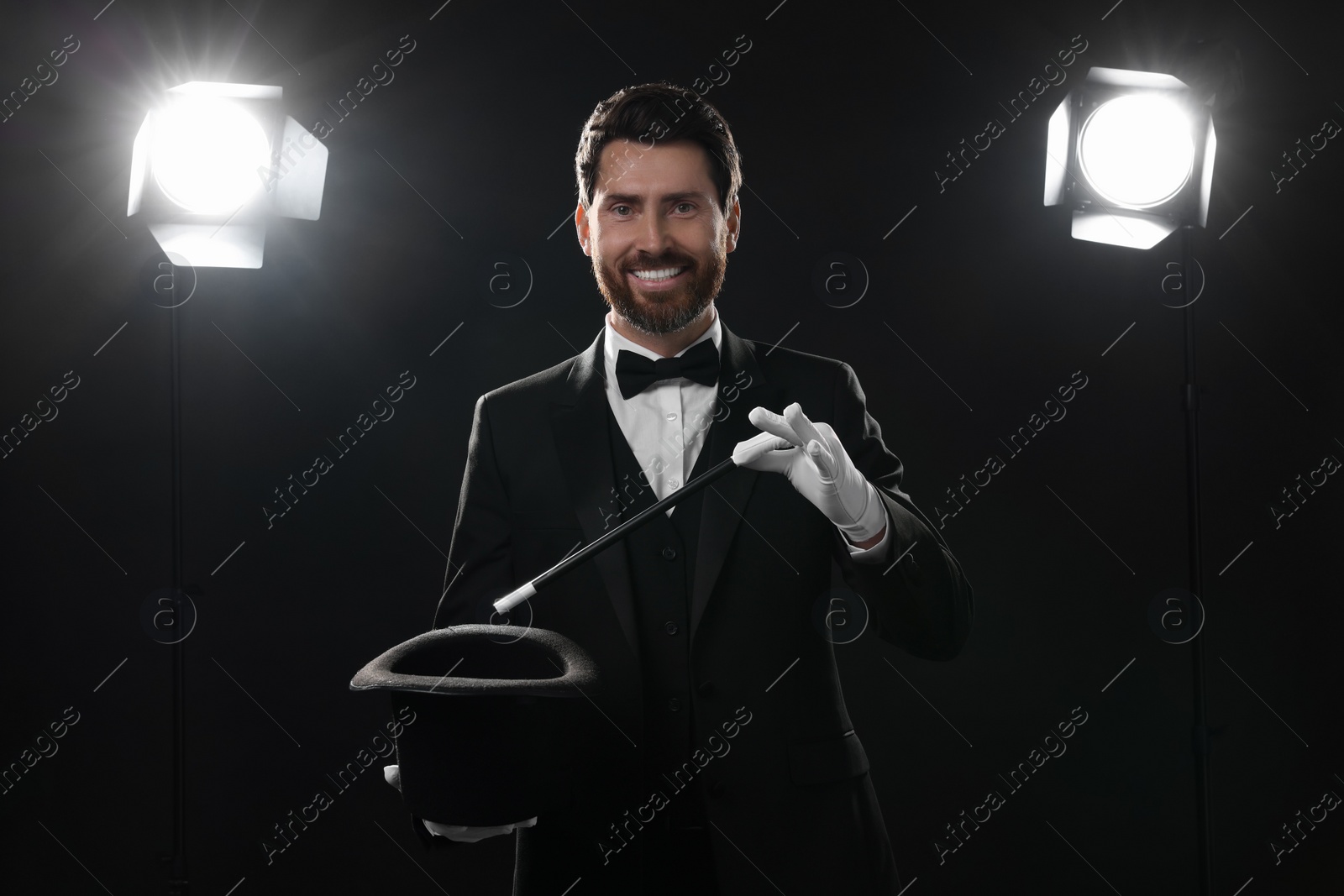 Photo of Happy magician showing magic trick with top hat on stage