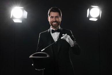 Happy magician showing magic trick with top hat on stage