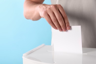 Photo of Man putting his vote into ballot box on light blue background, closeup. Space for text
