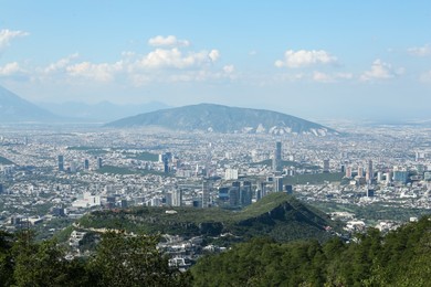 Picturesque view of city with trees, mountains and buildings under beautiful sky