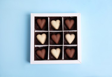 Photo of Tasty heart shaped chocolate candies on light blue background, top view. Happy Valentine's day