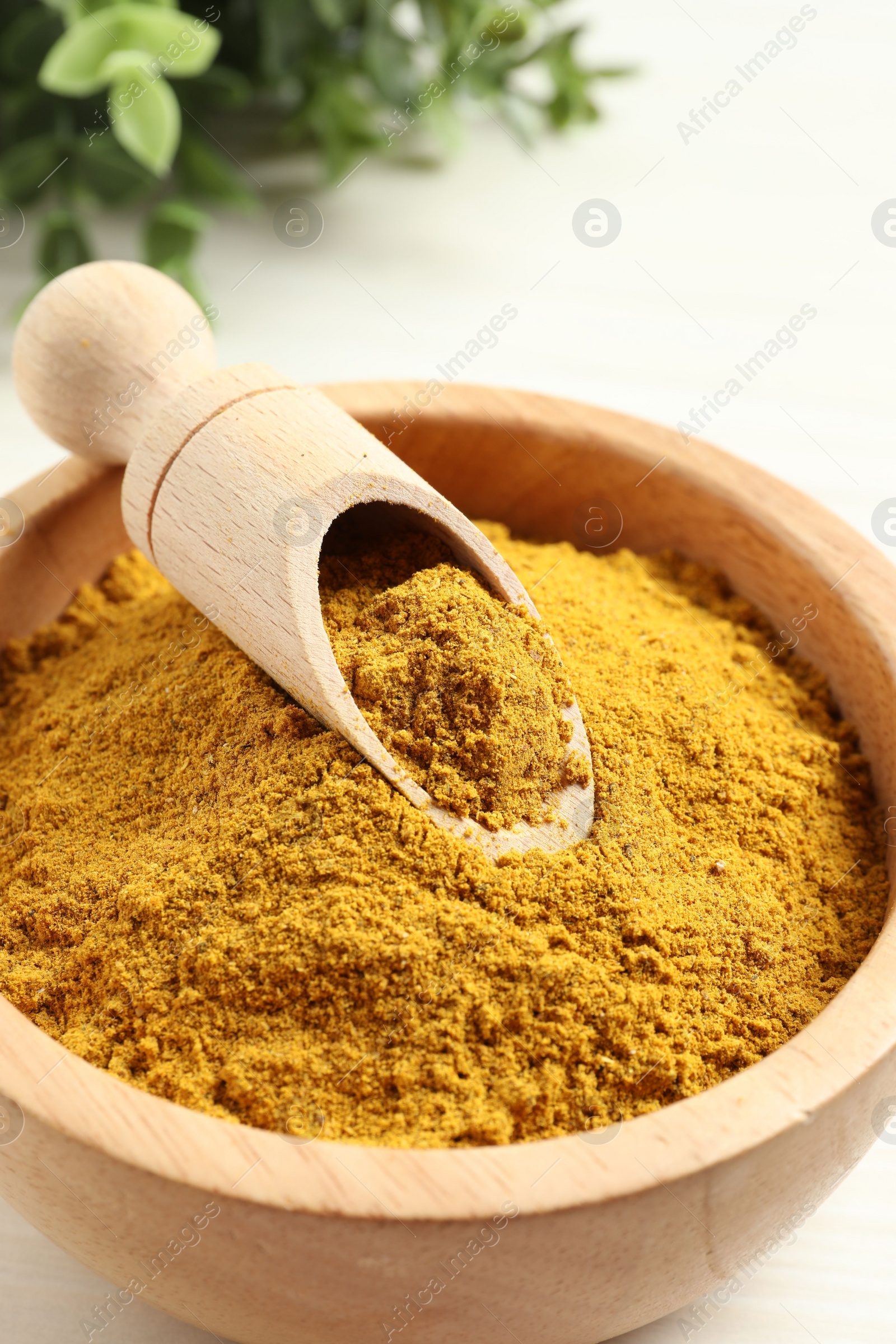 Photo of Dry curry powder in bowl and scoop on light table, closeup