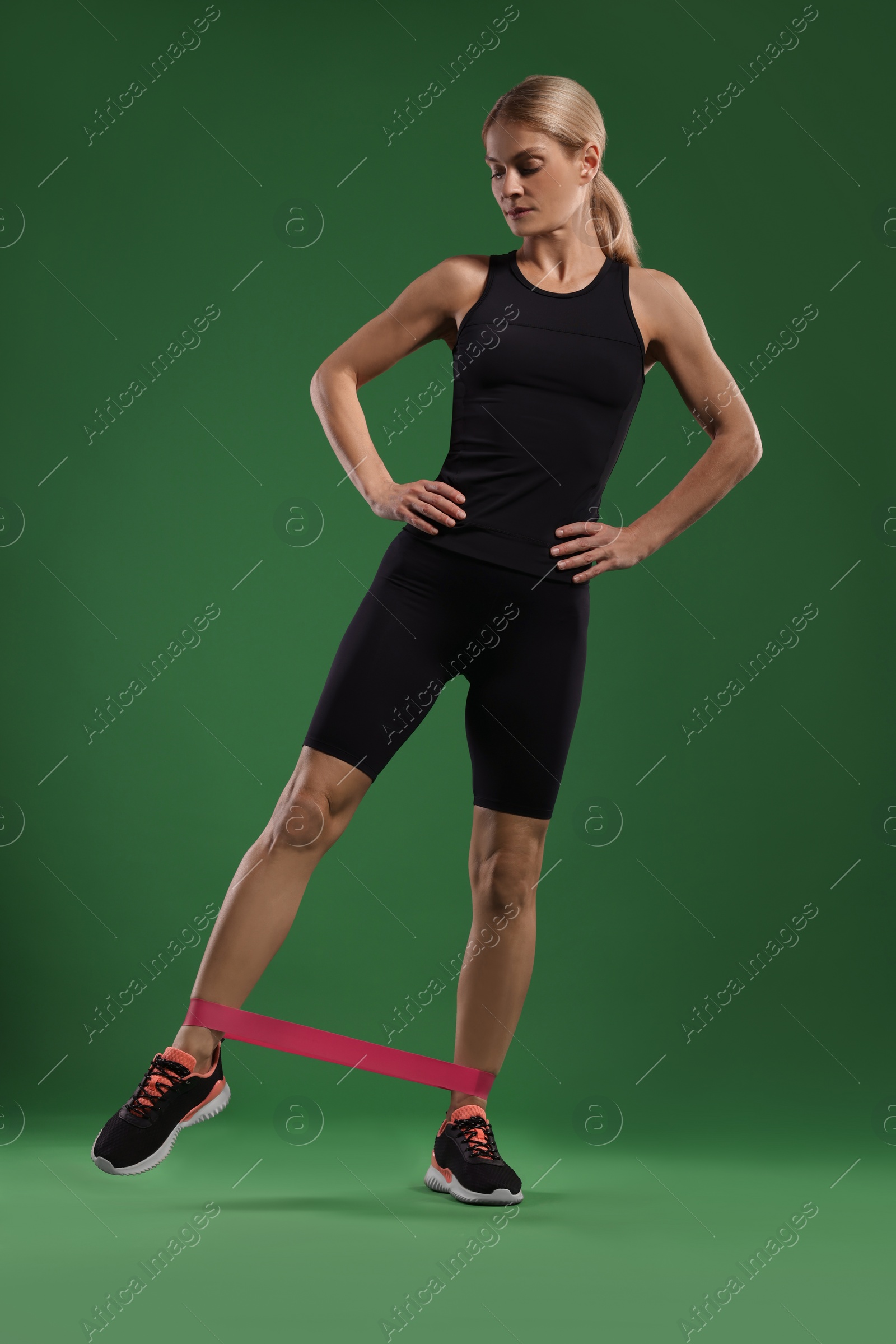 Photo of Athletic woman exercising with elastic resistance band on green background