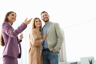 Photo of Female real estate agent showing new house to couple, indoors