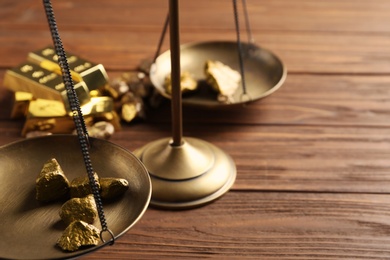 Photo of Scale pan with gold lumps on wooden table, closeup. Space for text