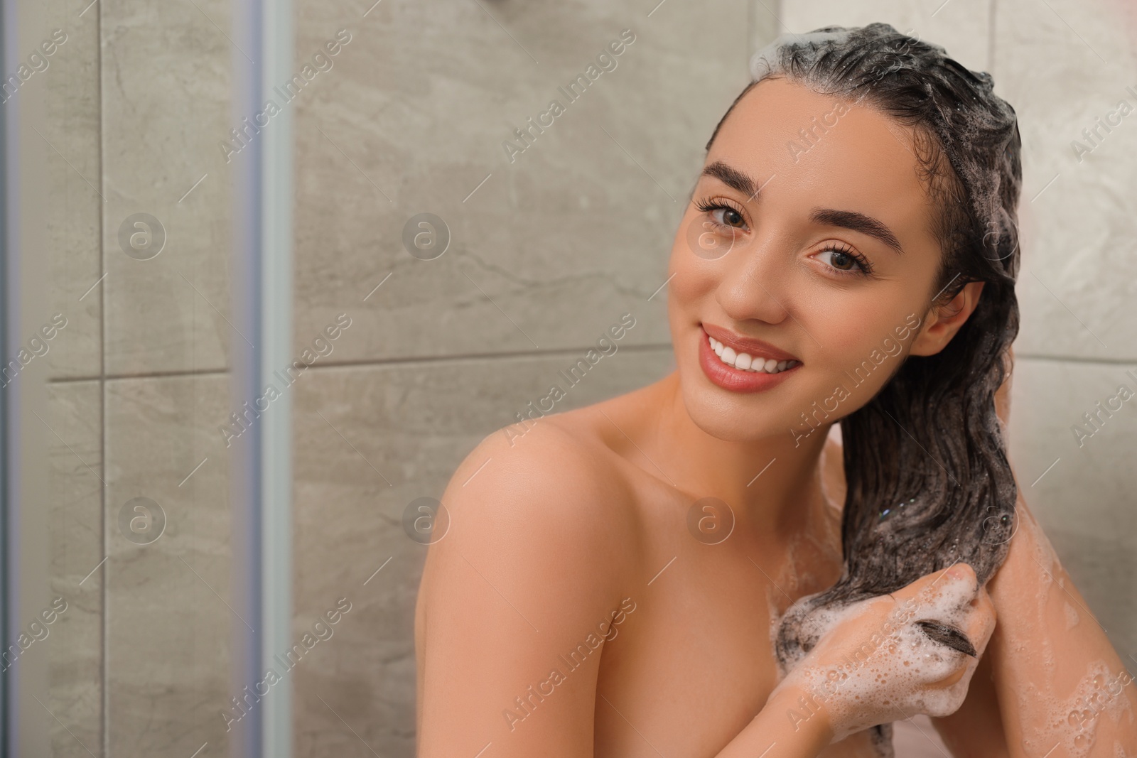 Photo of Happy woman washing hair with shampoo in shower. Space for text