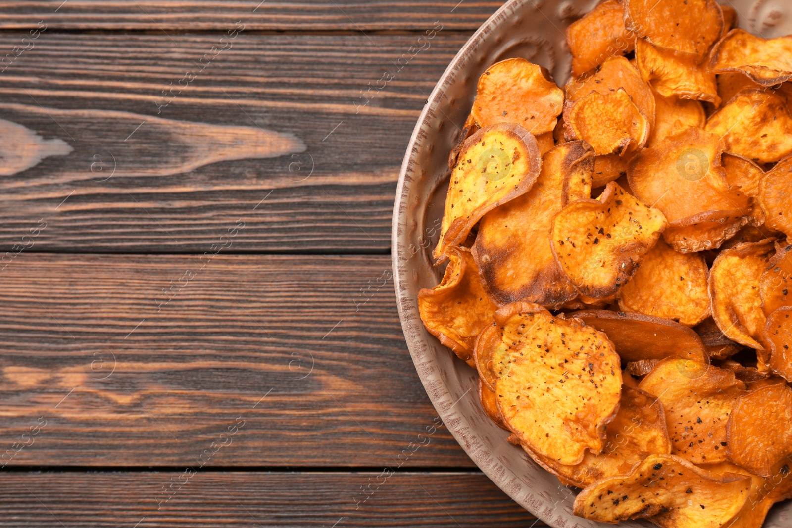 Photo of Plate of sweet potato chips on wooden table, top view. Space for text