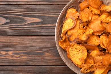 Plate of sweet potato chips on wooden table, top view. Space for text