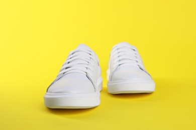 Pair of stylish white sneakers on yellow background