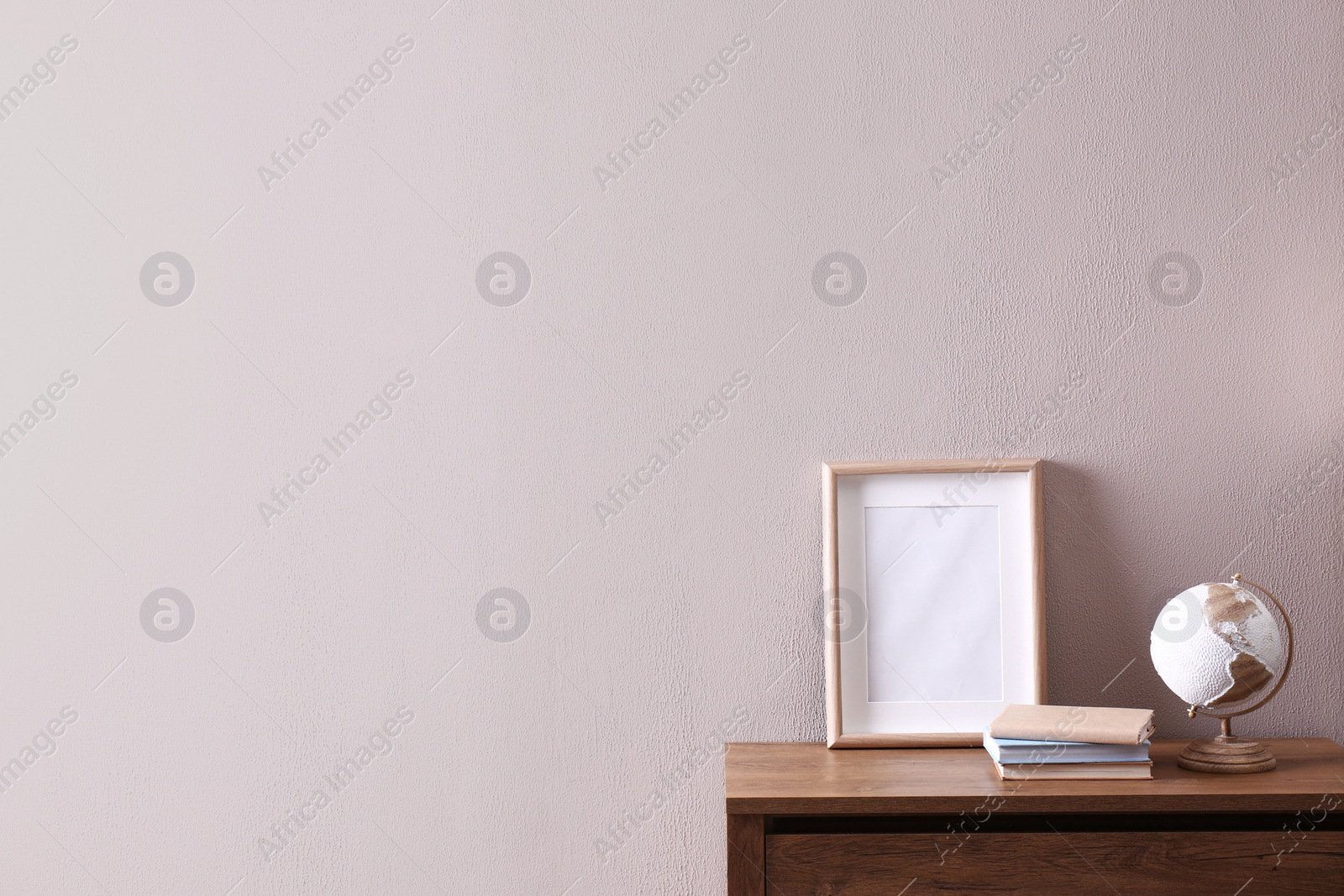 Photo of Wooden chest of drawers with globe, books and empty frame near beige wall in room, space for text. Interior design