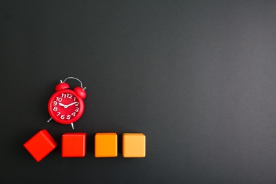 Alarm clock and colorful wooden cubes on black background, flat lay. Space for text