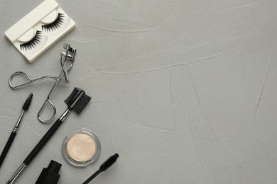 Photo of Flat lay composition with eyelash curler, makeup products and accessories on grey table. Space for text