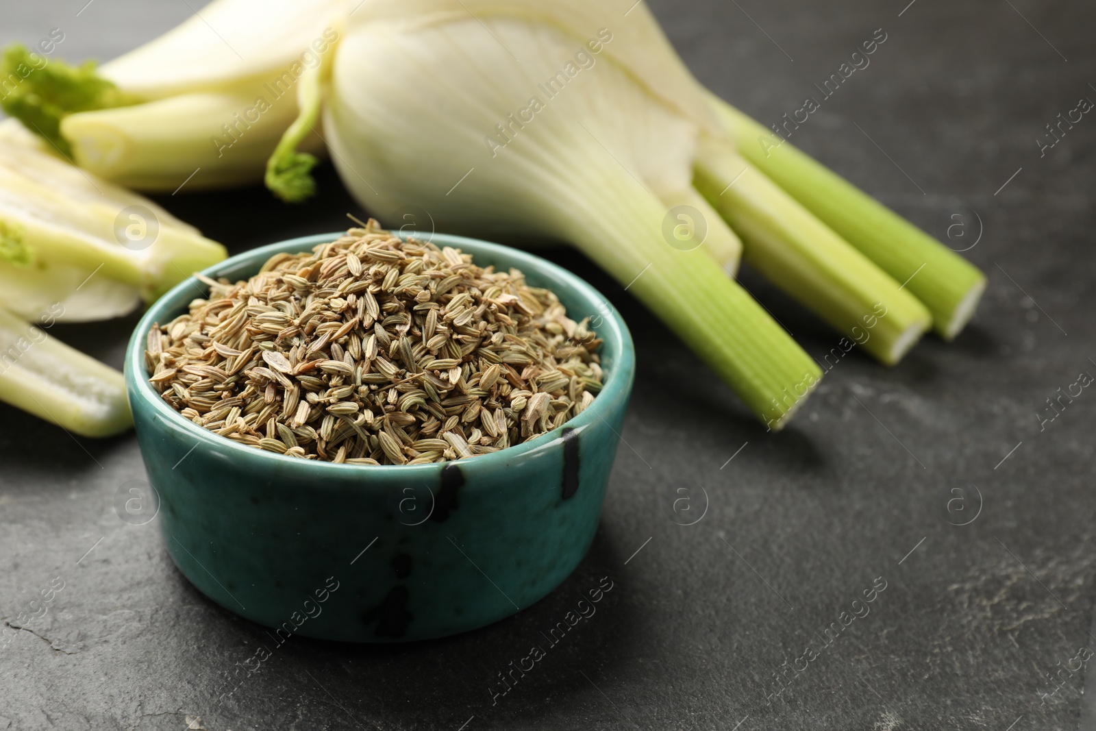 Photo of Fennel seeds in bowl and fresh vegetables on gray table, closeup