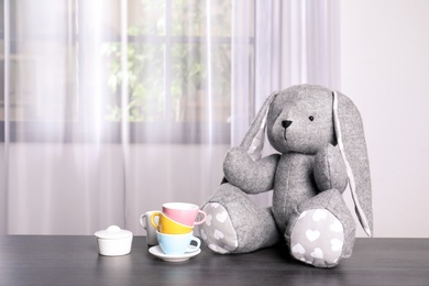 Photo of Adorable stuffed bunny and toy tableware on table indoors, space for text. Child room elements