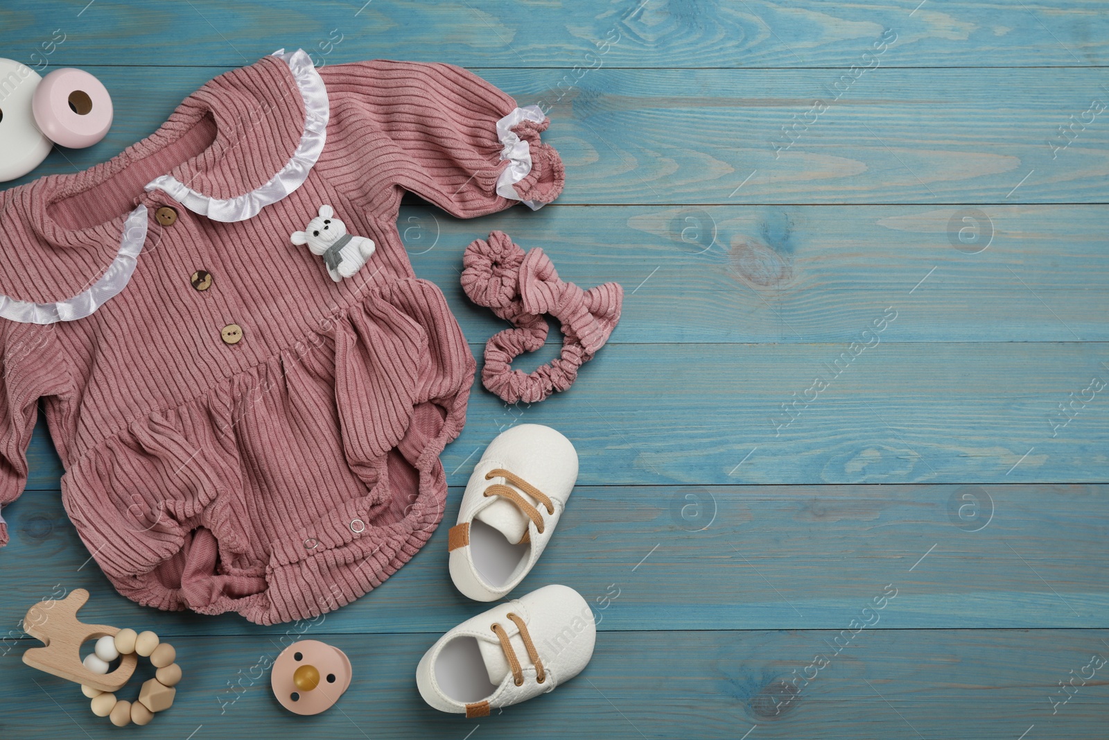 Photo of Flat lay composition with baby clothes and accessories on light blue wooden table. Space for text