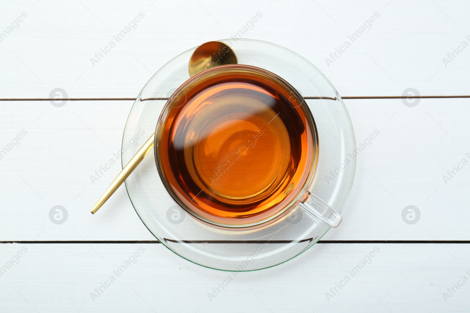 Photo of Glass cup of tea and spoon on white wooden table, top view