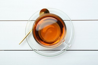 Glass cup of tea and spoon on white wooden table, top view