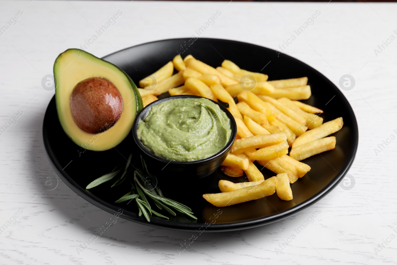 Photo of Plate with french fries, guacamole dip, rosemary and avocado served on white wooden table