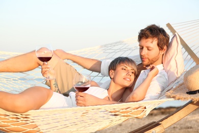 Photo of Young couple resting with glasses of wine in hammock on beach