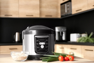 Modern multi cooker and ingredients on table in kitchen. Space for text