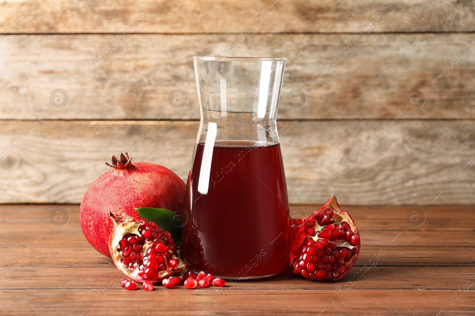 Photo of Jug of pomegranate juice and fresh fruits on table against wooden background