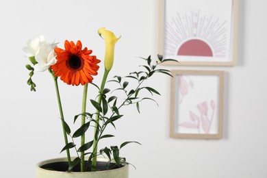 Stylish ikebana as house decor. Beautiful fresh flowers near white wall with pictures, space for text