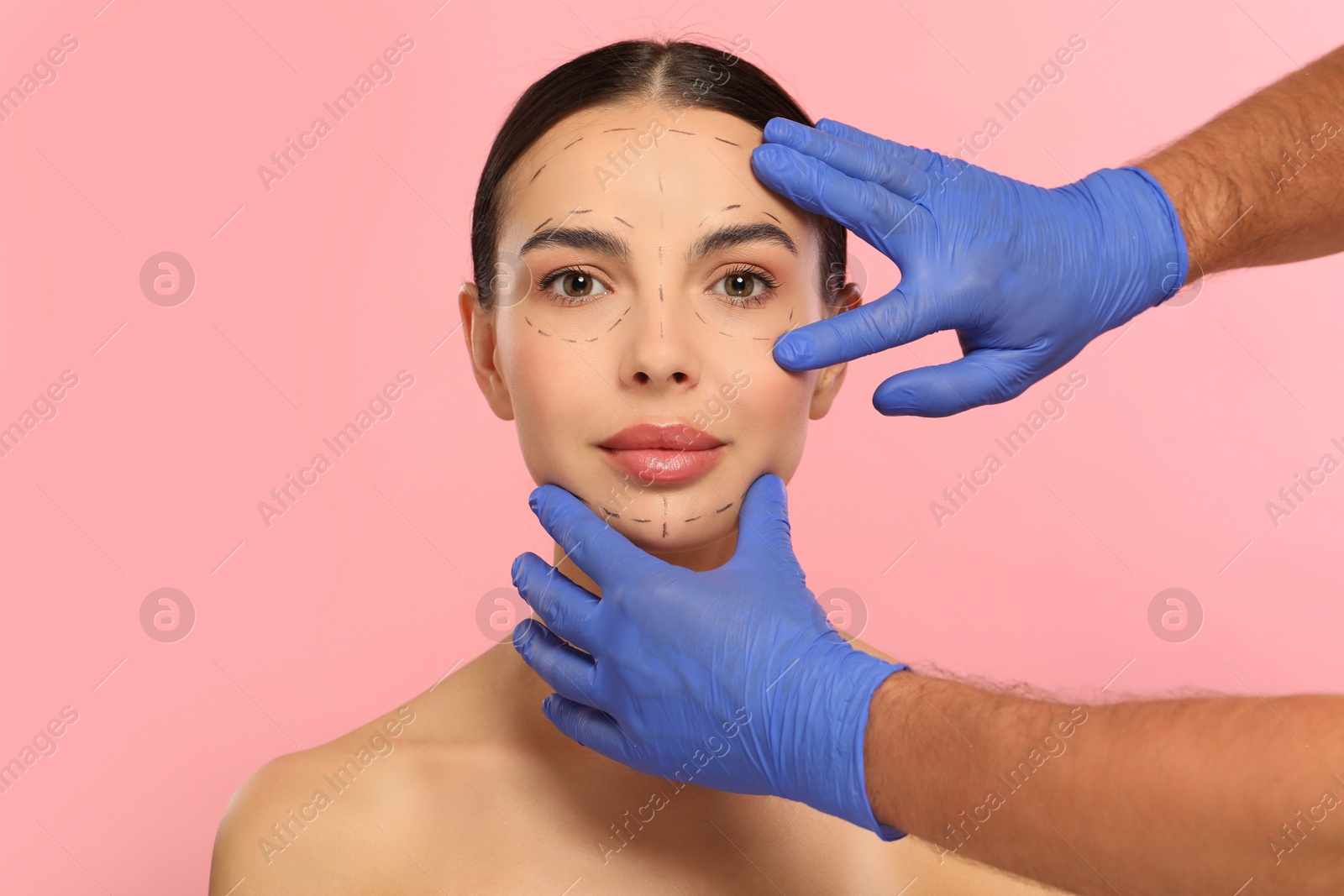 Photo of Doctor checking patient's face before cosmetic surgery operation on pink background