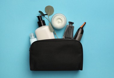 Preparation for spa. Compact toiletry bag with different cosmetic products on light blue background, flat lay