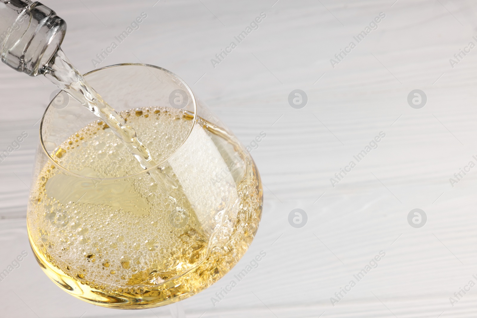 Photo of Pouring tasty aromatic wine in glass at white wooden table, closeup. Space for text