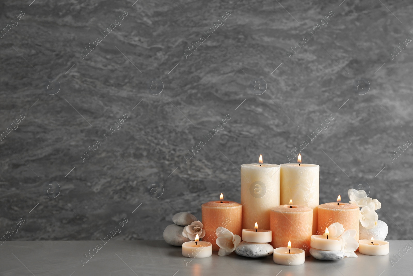 Photo of Beautiful composition with candles, flowers and stones on table against grey background. Space for text