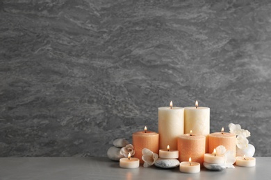 Photo of Beautiful composition with candles, flowers and stones on table against grey background. Space for text